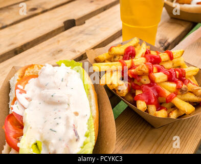 Plats à emporter avec un rouleau de homard aux frites ou aux frites avec ketchup et une demi-pinte de lager dans un verre en plastique sur une table de pique-nique extérieure Banque D'Images