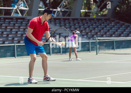 Joueur de tennis asiatique prêt à servir au début d'un match de double Banque D'Images