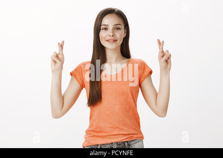 Fille priant son ami va gagner la compétition. Tourné à l'intérieur de certain bon-à la femme européenne en tee-shirt orange, élever les mains avec traversé finge Banque D'Images