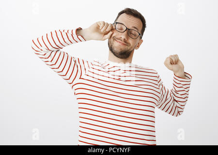 Portrait de sleepy assez heureux guy dans les verres, se frottant les yeux et un large sourire tout en s'étendant de l'épuisement, vouloir dormir après temps de travail Banque D'Images