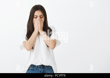 Studio shot of woman in casual allergique fatigué t-shirt et jeans, couvrant la bouche avec palmiers et de fermer les yeux tandis que les éternuements de l'allergie, redevance sentiment Banque D'Images