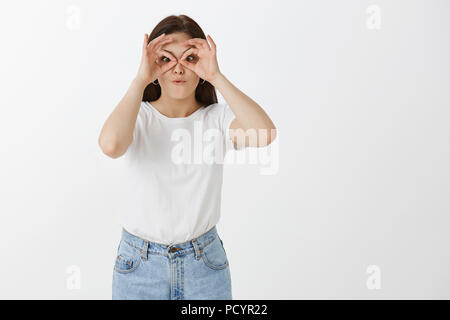 Heureux et joyeux femelle européenne freelancer en jeans et t-shirt blanc, faisant de cercles avec les mains sur les yeux comme si montrant des lunettes ou lunettes, singeant une Banque D'Images