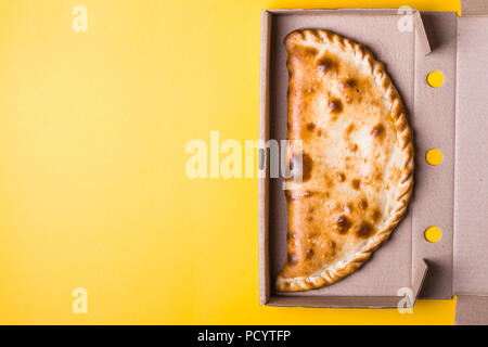 Calzone pizza fermé dans son emballage sur fond jaune. Banque D'Images
