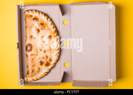 Pizza calzone fermée dans un emballage sur un fond jaune. Banque D'Images