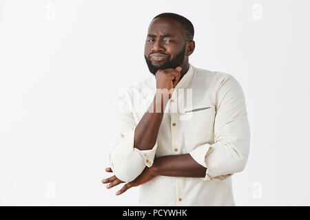 Nah, pas impressionnant, en doute. Pas mécontent de belles emotive African American man en chemise blanche, holding de poing sur le menton et les sourcils avec Banque D'Images