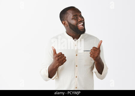 Capture d couverte d'humour et d'émotion joyeuse de peau foncée avec guy beard dans le quartier branché d'outfit, showing Thumbs up et tourner le visage à l'appareil photo, tout sourire, li Banque D'Images