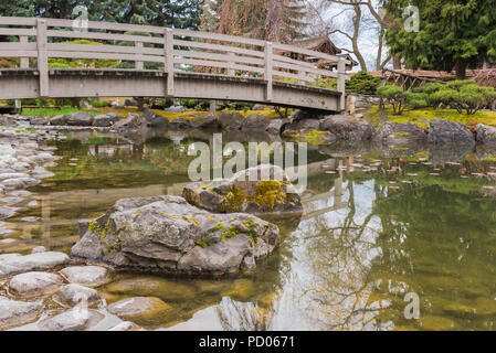 Les roches moussues et pont sur l'étang de koi Kasugai à jardins, une ville populaire Park dans le centre-ville de Kelowna, BC, Canada Banque D'Images