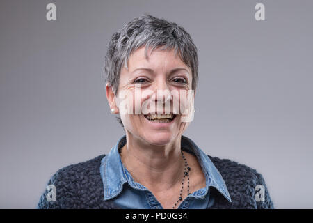 Smiling happy femme plus âgée avec des cheveux courts donnant l'appareil photo un sourire amical isolé sur gray Banque D'Images