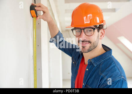 Portrait de jeune homme à l'aide de ruban à mesurer tout en travaillant sur chantier de construction. Banque D'Images