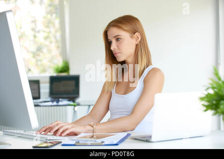 Belle jeune femme d'adjointe aux ventes de la saisie sur clavier de l'ordinateur au bureau. Banque D'Images