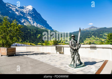 Statue d'un skieur dans le centre du village de Grindelwald, l'Eiger en arrière-plan, sur une journée ensoleillée avec un ciel bleu clair Banque D'Images