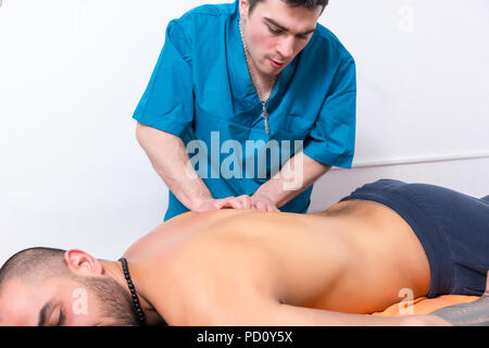 Masseur kinésithérapeute ou faire un massage dos manipulant les muscles d'un patient allongé sur une table dans un close up portrait Banque D'Images