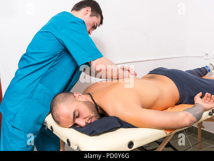 Homme Massothérapeute Redonner Polissez pour clients masculins Lying on stomach sur table de massage en clinique Banque D'Images