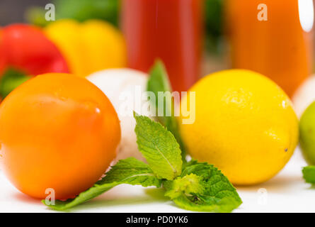 Tige de menthe avec du citron et tomate affichée sur une surface blanche avec des verres de jus ou smoothies et un assortiment de fruits et légumes frais ingrédients Banque D'Images