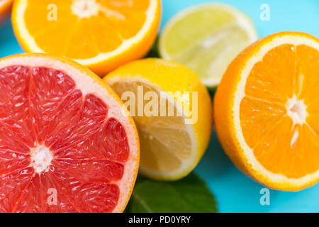 Moitié de pamplemousse, orange, citron et lime dans une vue en gros plan sur un fond bleu avec l'accent sur le Pamplemousse ruby Banque D'Images