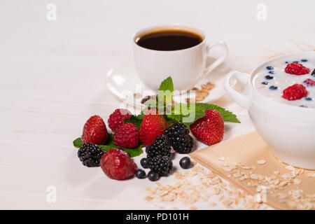 Un assortiment de baies fraîches, y compris les bleuets, mûres, framboises et fraises, sur la table du petit déjeuner avec café et céréales avec lait Banque D'Images