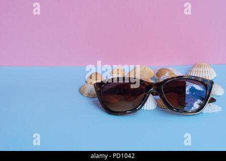 Différents types d'obus et l'un des lunettes de soleil sur un fond rose et bleu clair. Image minimaliste qui capture l'esprit de l'été. Tube Acanthocardia Banque D'Images