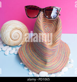 A women's sunglasses sur une grande Dorades de mer et plusieurs petites coquilles sur un fond bleu et fuchsia. Nice minimaliste qui capture l'image Banque D'Images