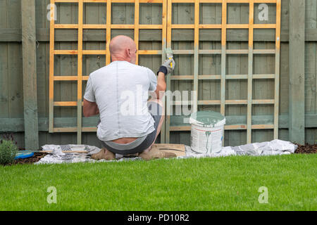 L'homme accroupi et peinture d'un treillis de jardin Banque D'Images