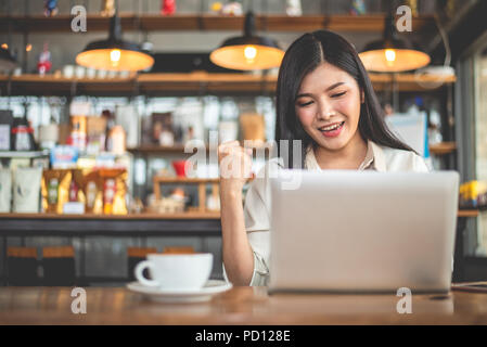 Asian female freelancer faisant geste heureux en levant la main lors de l'utilisation d'ordinateur portable dans un café. Succès d'affaires et de concept. Café en plein air et de thème. C Banque D'Images