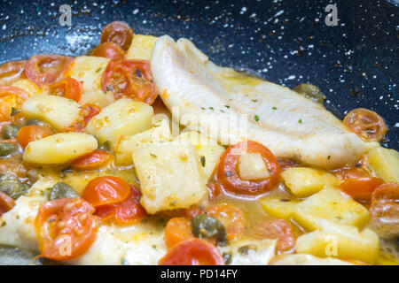 Cabillaud cuit dans une casserole, avec de la tomate, les pommes de terre et les câpres Banque D'Images