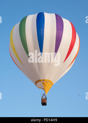 Un ballon à air chaud à rayures colorées en vol contre ciel bleu. Photographié à partir de ci-dessous. Banque D'Images