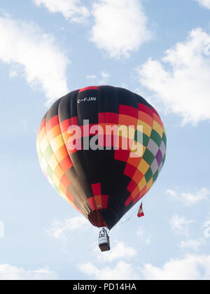 Un noir, rouge, orange et jaune avec motif géométrique ballon en vol au Big Sky Balloon Fest avec le pilote et un passager visible. Banque D'Images