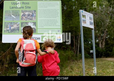 Deux filles d'oeil à un Booroona signe landcare, piste de marche sur la Ross River, Rasmussen, 4815 Australie QLD Banque D'Images