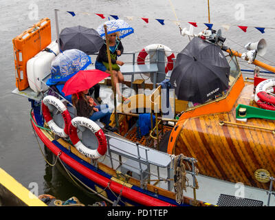 Les passagers sur l'ancien Whitby Lifeboat "Mary Ann Hepworth' dans le port de Whitby en attente d'aller sur un voyage de plaisir d'été jusqu'parapluies en cas de pluie Banque D'Images