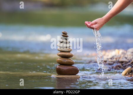 Close-up résumé image de femme part verser de l'eau sur les différentes tailles inégales brun naturel et la forme des pierres comme équilibrée pile pyramide monument Banque D'Images