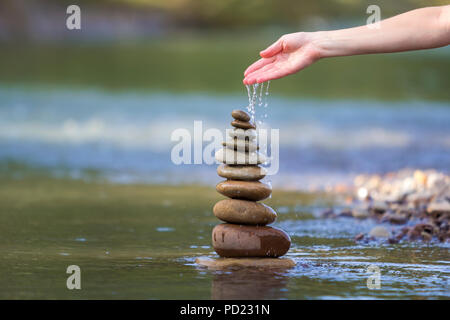 Close-up résumé image de femme part verser de l'eau sur les différentes tailles inégales brun naturel et la forme des pierres comme équilibrée pile pyramide monument Banque D'Images