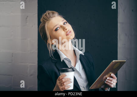 Femme élégante habillés en costume et une blouse qui pose à l'appareil photo avec café et tablette. Temps libre. close up de droit Banque D'Images