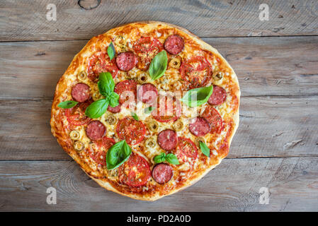 Pizza italienne avec des tomates, de salami, fromage, olives vertes et les feuilles de basilic sur table en bois. Des pizzas fraîches, copiez l'espace. Banque D'Images