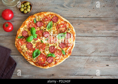 Pizza italienne avec des tomates, de salami, fromage, olives vertes et les feuilles de basilic sur table en bois. Des pizzas fraîches, copiez l'espace. Banque D'Images