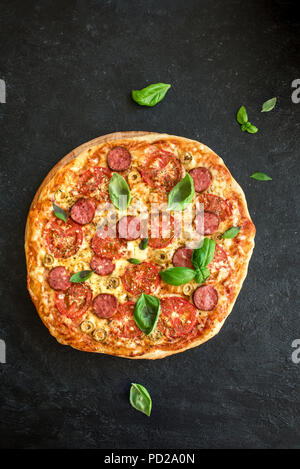 Pizza italienne avec des tomates, de salami, fromage, olives vertes et les feuilles de basilic, vue du dessus sur noir. Des pizzas fraîches, copiez l'espace. Banque D'Images