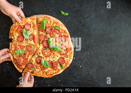 Les gens en tenant les mains des tranches de pizza italienne. Pizza italienne et les mains close up sur fond noir, vue du dessus, copiez l'espace. Banque D'Images