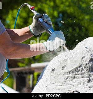 Jeune homme au travail à l'air comprimé le ciseau et des gants protecteurs pour taille un bloc de pierre Banque D'Images