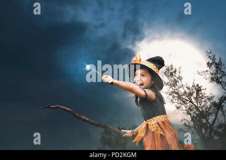 Cute asian petite sorcière fille avec baguette magique sur ses mains sur fond de nuit Banque D'Images