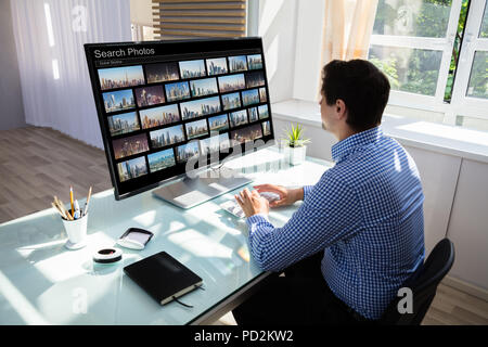 Jeune homme recherche éditeur de photos sur computer in office Banque D'Images