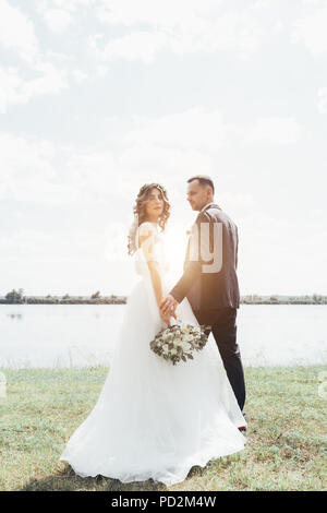 Tenue de mariage en couple avec un bouquet de fleurs et de verdure est dans les mains sur la toile de fond le terrain au coucher du soleil, la mariée et le marié. Banque D'Images