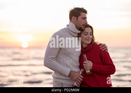Jeune couple hugging et boire de la bière sur le coucher du soleil au cours de l'automne temps at beach Banque D'Images