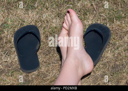 Paire de pieds avec des tongs sur certains herbe brûlée pendant une vague de détente confortable. les chaussures. Banque D'Images