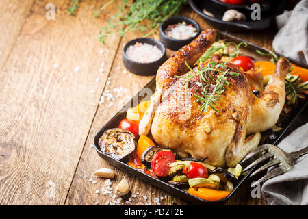 Poulet entier cuit au four avec légumes et herbes close-up sur une plaque sur une table. Banque D'Images