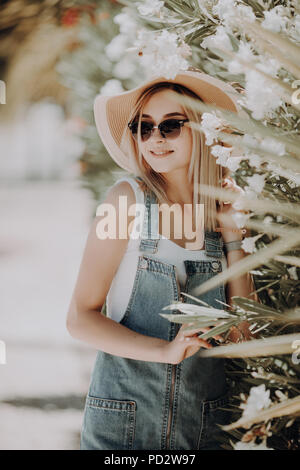 Portrait d'une belle femme en chapeau de paille près d'arbres en fleurs blanc sur la rue Banque D'Images