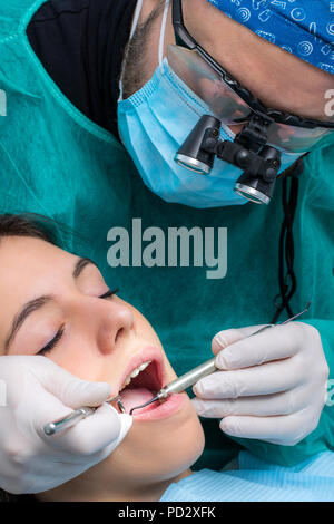 Close up of dentiste portant des loupes médicales travaillant sur female patient.chirurgien en robe verte avec miroir de la bouche et scaler. Banque D'Images