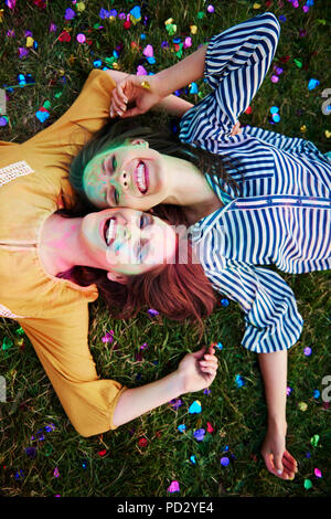 Deux jeunes femmes couvertes en poudre de craie de couleur étendu sur l'herbe à au Festival de Holi, portrait Banque D'Images