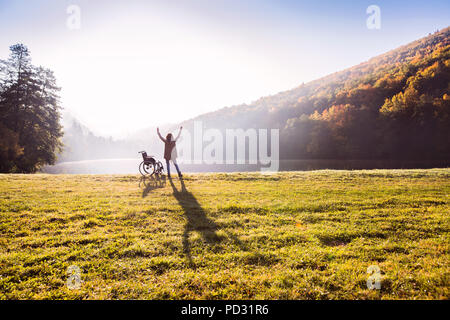 Senior woman standing par le fauteuil roulant à l'automne la nature. Banque D'Images