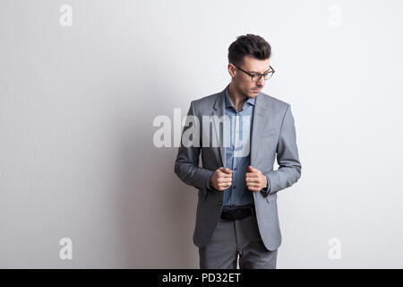 Portrait d'un jeune homme avec des lunettes dans un studio, habillé en costume gris. Banque D'Images