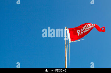 Danger pour la baignade. Drapeau d'avertissement rouge sur une plage en agitant au-dessus de ciel bleu Banque D'Images