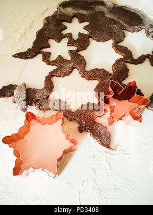 Close-up de deux emporte-pièces en cuivre en forme de flocons de neige, sur un fond blanc avec de la farine autour, et des matières gingerbread dough. Banque D'Images